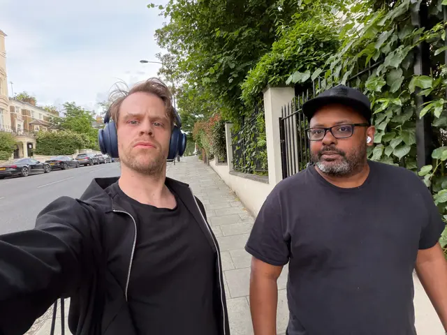Zwei Männer auf einem Gehweg in einer von Bäumen gesäumten Londoner Wohnstraße.