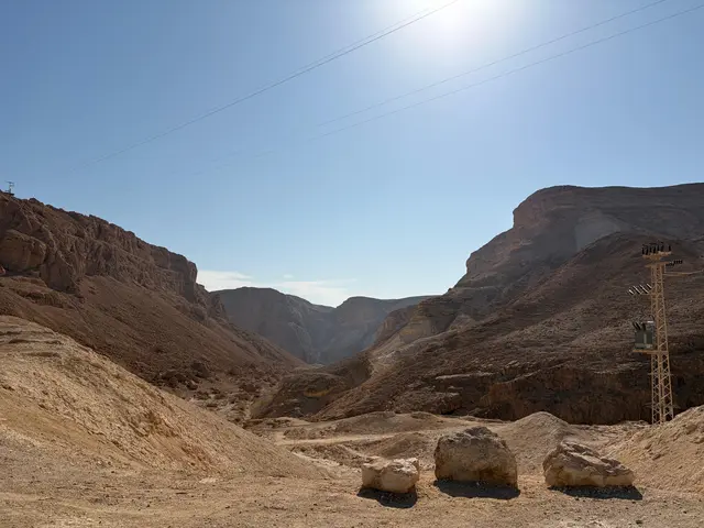 Blick in ein weites Wüstental bei Masada mit steilen, rotbraunen Felshängen unter wolkenlosem blauem Himmel.