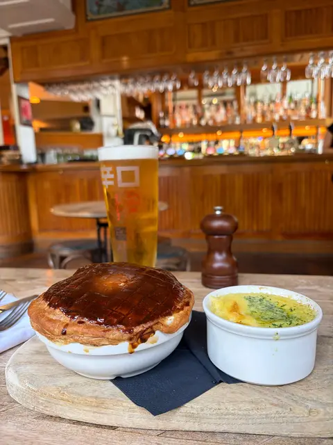 Ein Fleischpie mit knuspriger Kruste, dazu Kartoffelpüree und ein Glas Bier auf einem Holzbrett in einem Pub.