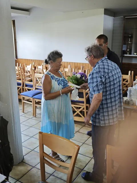 Links steht Gabriela Placzek, rechts daneben Eugenio Maiolo, dahinter Manuel Diefert im Vereinsheim des KGV Dornröschen während der Blumenübergabe.