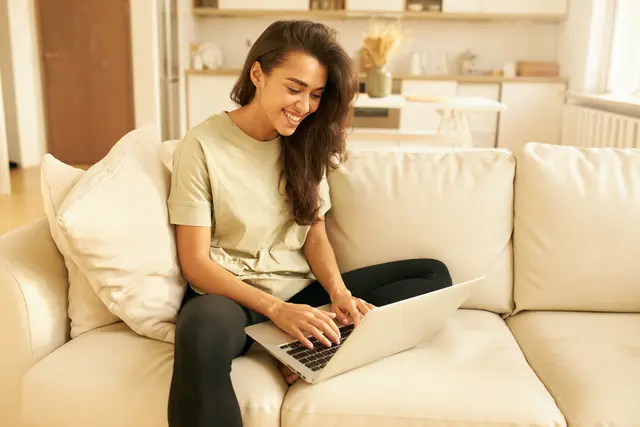 Eine Frau sitzt gemütlich auf der Couch und nutzt ihren Laptop für Hobbys und Online-Shopping. Entspanntes Surfen im Netz und digitale Kommunikation von zu Hause aus. | Foto: Adobe Stock | shurkin_son