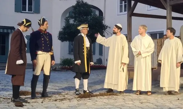 Mönche erzählen Beamten von Klostergeschichte, welche den Plänen entgegenstehen, ohne Sie zum davon Ablassen bewegen zu können 