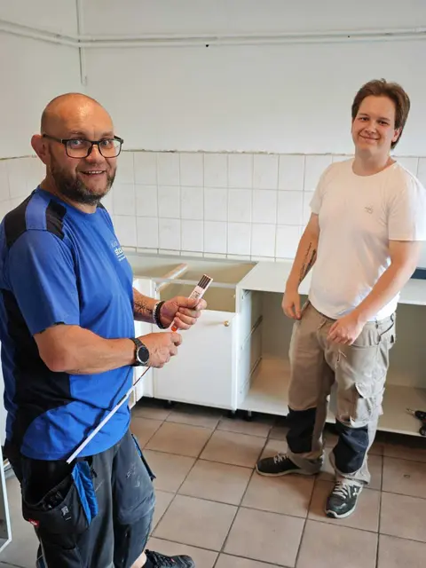 Zwei Personen arbeiten in einer Küche und bereiten den Aufbau der neuen Küchenelemente vor.