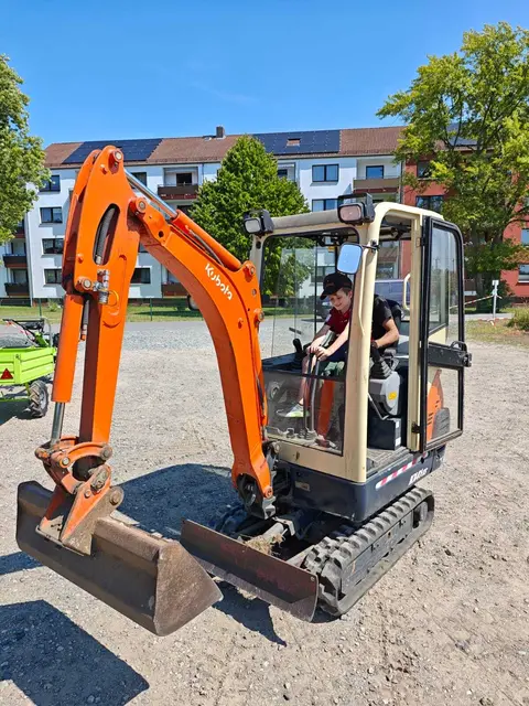 Ein Kind sitzt in einem Minibagger und fährt das Fahrzeug zum ersten Mal auf einer Baustelle.