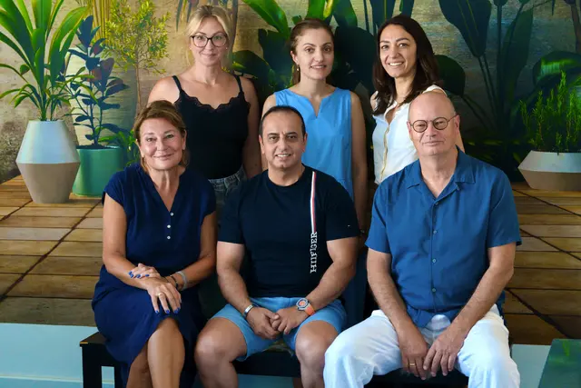 Gruppenfoto mit sechs Personen vor einer blauen Wand mit Pflanzen – Tamer Ghazal in der Mitte vorne