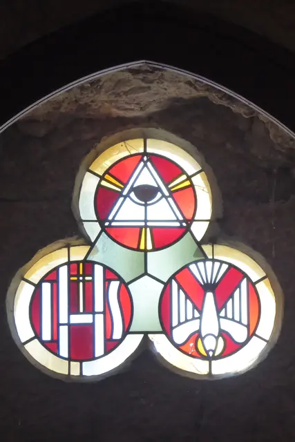 In den drei miteinander verbundenen Rundfenstern über dem Haupteingang der Kirche sind christliche Symbole zur Darstellung der Dreifaltigkeit (Trinität) zu sehen: Das Auge der Vorsehung (Auge im Dreieck oben) steht für Gott, den alles sehenden Vater. Das Monogramm IHS (unten links) symbolisiert Jesus Christus. Die Taube (unten rechts) stellt den Heiligen Geist dar. 