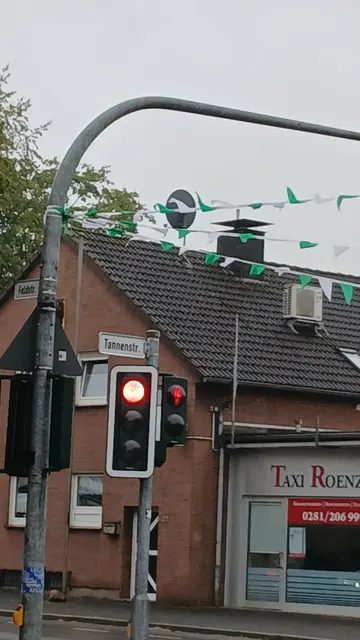 Schützenfest-Girlanden über der Straßenkreuzung Feldstraße/Tannenstraße in Wesel-Obrighoven. Weiß Grüne Girlanden (Wimpelketten) befestigt am Ampelmast. | Foto: Siegmund Walter, 18.08.2026