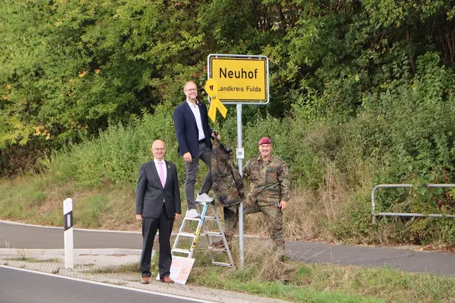 Der Parlamentarische Staatssekretär Michael Brand, Bürgermeister Heiko Stolz und Oberst der Reserve Christoph Seifert (von links) befestigen die gelbe Schleife an einer der Ortseingangstafeln. | Foto: Förderverein Stab DSK e.V. 