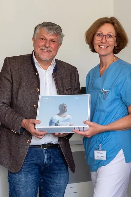 Auf dem Foto sind Bernd Müller und Dr. Marleen Pfeiffer zu sehen, die ein in einem Karton verpacktes Schlafapnoe-Diagnosegerät in der Hand halten