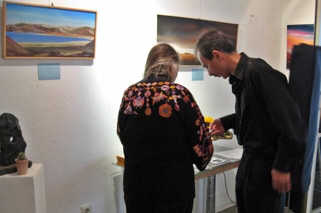 Zum Abschluss der Vernissage übergab die Künstlerin, die auch Schriftstellerin ist, eines ihrer Märchenbücher mit Widmung an Arkadi Spektor als Dank für sein Konzert. Im Hintergrund Gemälde von Thomas Hillenbrand links "Totes Meer I"