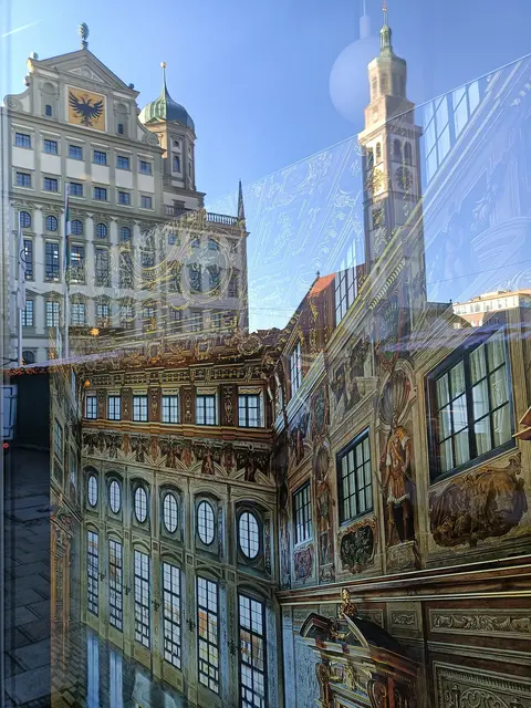 Im Schaufenster sieht man ein Bild des "Goldenen Saals", der sich im Rathaus im Hintergrund befindet. Daneben der jetzt eingerüstete Perlachturm.