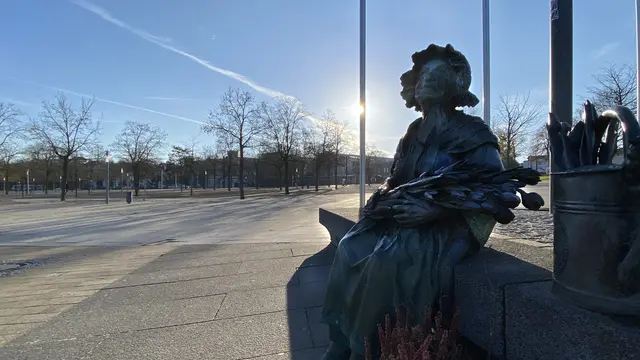 Ein Denkmal auf dem Platz in der Nähe des Burgsees erinnert an Schwerins Ehrenbürgerin, an die Blumenfrau Bertha Klingberg (1898 – 2005). Der Platz trägt ihren Namen („Bertha-Klingberg-Platz“). Es wird darauf hingewiesen, dass sie 1990 innerhalb kürzester Zeit rund 17.000 Unterschriften zugunsten von Schwerin als Landeshauptstadt des seinerzeit neuen Bundeslandes Mecklenburg-Vorpommern gesammelt hatte. Der Bildhauer Bernd Streiter gestaltete 2010 das Bertha-Klingberg-Denkmal. Foto: Helmut Kuzina