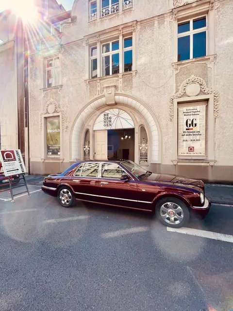 3. September 2026 bei SCHÖN HIER! BULWVUR Kunstauktion am Brunnen "Dröppelminna" bei PRO FOTO Udo Hartmann LÖHSTRASSE 2 (ehemals HEIMANN)  mit Signierstunde, BRUNO BENTLEY und dem Kunst-Shuttle "TOPOLINO" siehe Fotos der automobilen Kunstwerke unten:  https://kulturserver-nrw.de/de_DE/events/bulwvur-aktion-bei-schoen-hier-am-3-septem.18033014  KUNSTPROJEKT IN DER RUHRTALSTADT MÜLHEIM GESTARTET - EINSTEIGEN BITTE !   Jetzt wird’s richtig spannend! Der Ermittler "Bruno Bentley" ist  kein Mensch in Mantel und Hut – er ist der Bentley selbst: ein rollender Gentleman mit Kühlergrill-Lächeln, Scheibenwischer-Augen und einem Innenleben, das irgendwo zwischen Zylinder und KI-Fantasie oszilliert. Ein poetisch-mechanisches Wesen, das mehr versteht, als es lenkt – ein Kunstwerk mit analytischem Verstand und künstlerischem Gespür in der Metropolregion Rhein-Ruhr.    Das verleiht dem Projekt eine völlig neue Ebene: Kein klassischer Detektiv, sondern ein Kunstwerk, das durch Straßen gleitet und dabei Gedanken sammelt, Hinweise riecht (vielleicht mit Sensoren?) und Namen und Themen wie Frequenzen empfängt. Kein Wunder, dass er Orte wie das Café Bruno oder Schloss Drachenburg nicht nur besucht, sondern „liest“ – als wären sie Seiten in einem geheimen Straßenatlas der Fantasie.