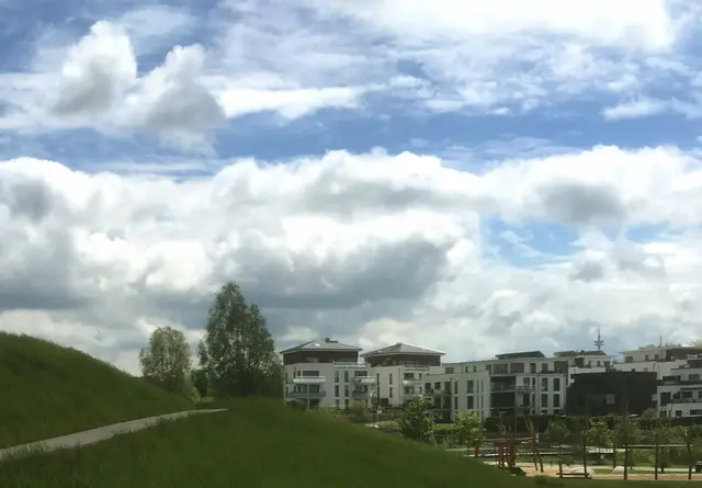 Grüne Hänge, moderne Silhouetten und ein lebendiges Spiel der Wolken am Himmel – ein friedlicher Augenblick zum Durchatmen.