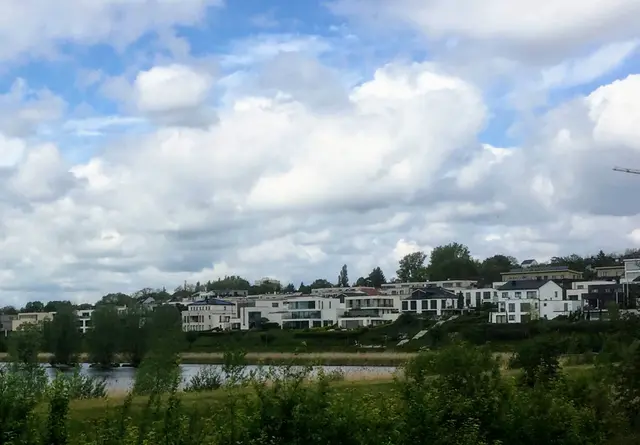 Wasser im Vordergrund, helle Fassaden am Hang und ein weiter Wolkenhimmel – ein ruhiger Augenblick voller Raum und Weite.